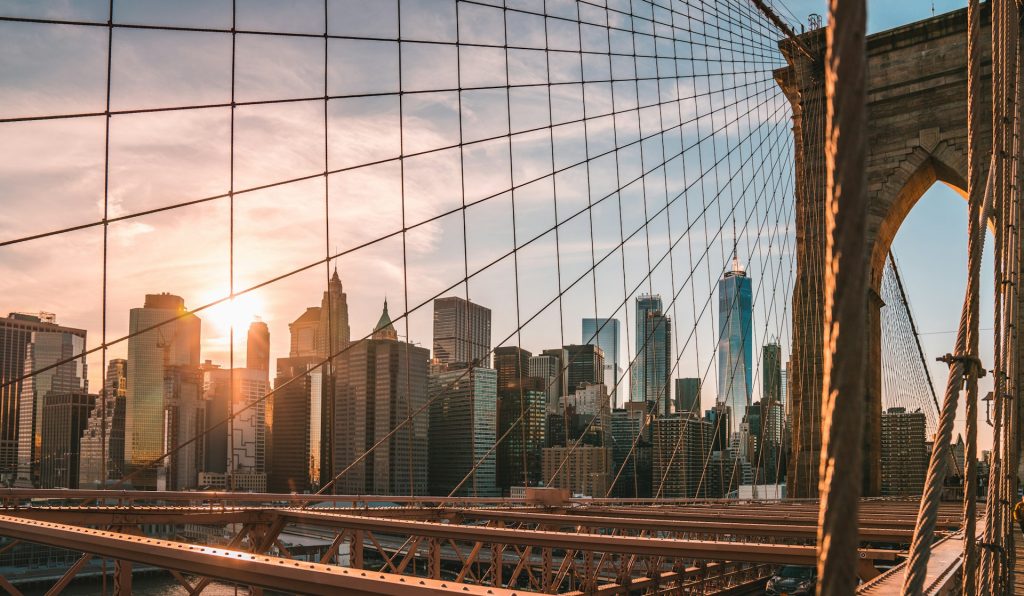 Il ponte di Brooklyn illuminato dal tramonto, con il cielo colorato e le silhouette degli edifici di New York sullo sfondo.