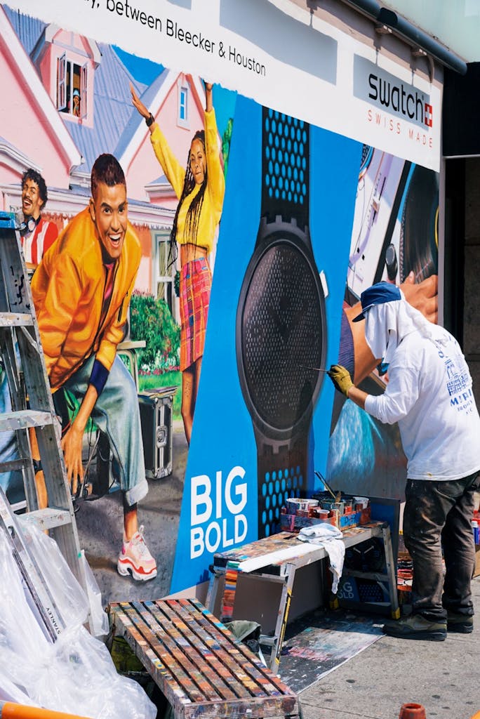 A street artist creates a vibrant mural in an urban setting near Swatch store.