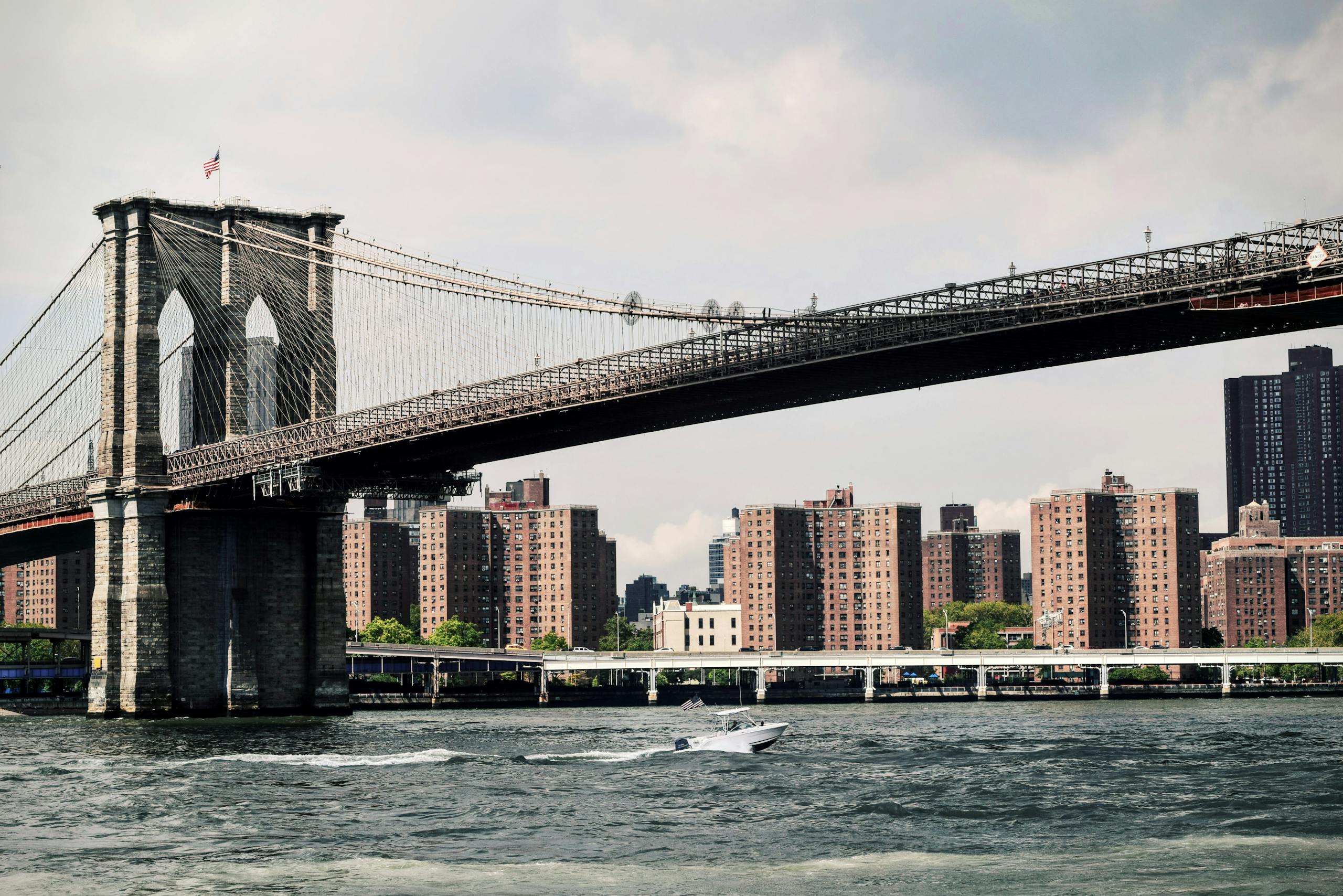 View of the Brooklyn Bridge with New York cityscape and river in daylight.