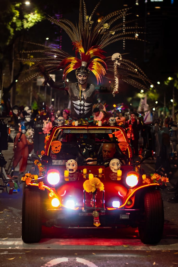 Colorful Day of the Dead parade with decorated car and dancers in costumes at night.