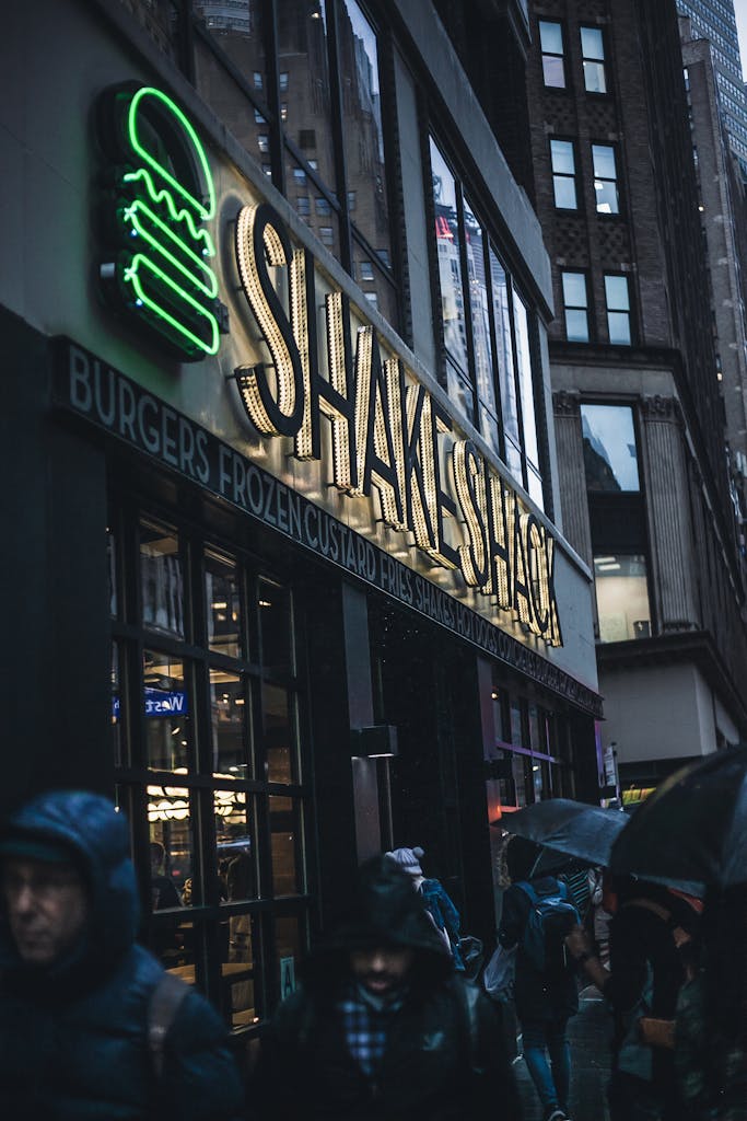 Street scene of Shake Shack in Times Square at night during rain, capturing city life.