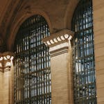 From below of illuminated interior of Grand Central Terminal station with high decorated ceiling and big windows with pillars in New York USA