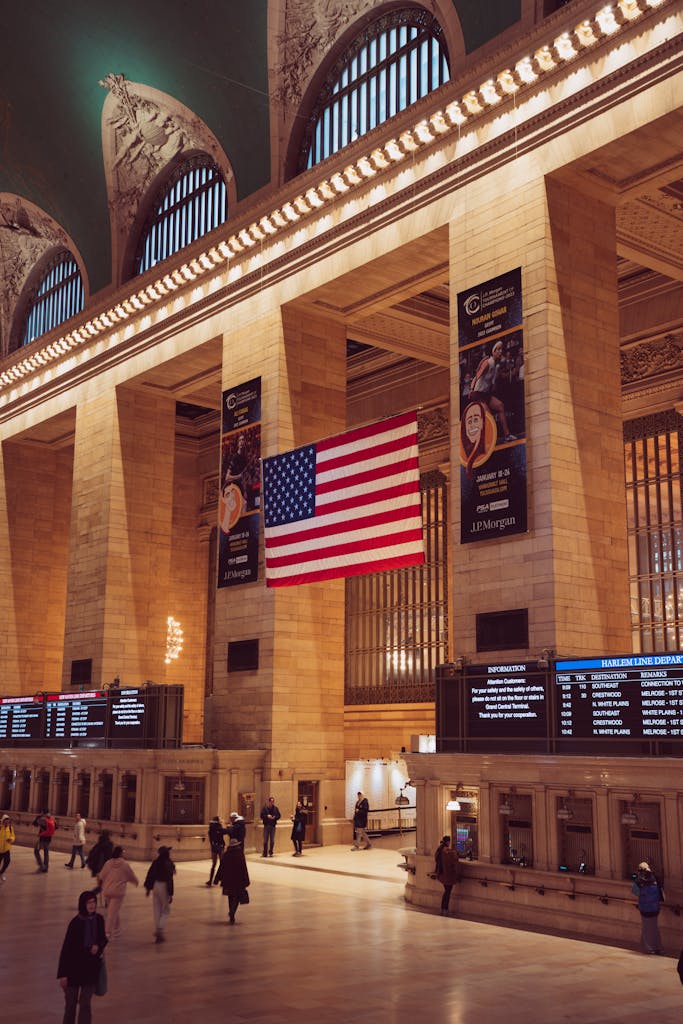 Interior of Grand Central Terminal, NYC, featuring a large American flag and bustling travelers.