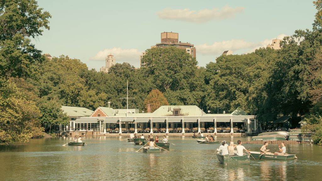 People enjoy a boat ride on the serene lake in Central Park, NYC, near the famous Boathouse.